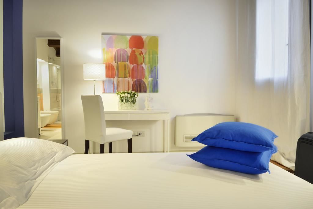 A hotel room with a bed, a desk, a chair, a lamp, and a colorful abstract painting on the wall.