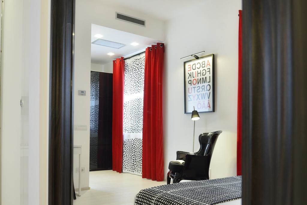 A modern hotel room with a bed, a chair, and a wall-mounted lamp.