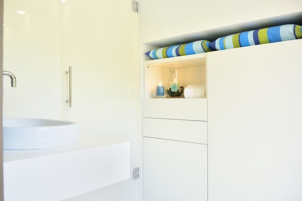 A bathroom with a white sink, a shower, and a storage cabinet with striped pillows.