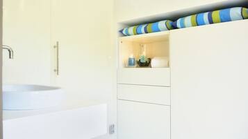 Une salle de bain avec un lavabo blanc, une douche et un meuble de rangement agrémenté de coussins à rayures.