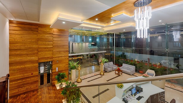 A modern hotel lobby with wooden paneling, a glass wall, a chandelier, and a seating area with a desk. - Hotel Lance International (Nagercoil)