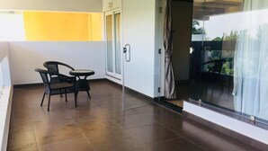 A balcony with a chair and table, a sliding glass door, and a view of greenery outside. - Hotel Lance International (Nagercoil)