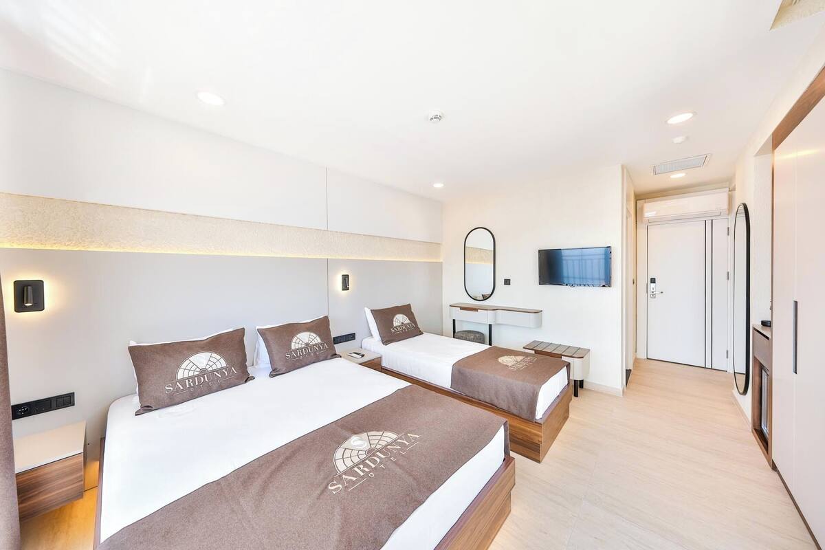 A hotel room with two beds, a TV, a mirror, and a wardrobe.