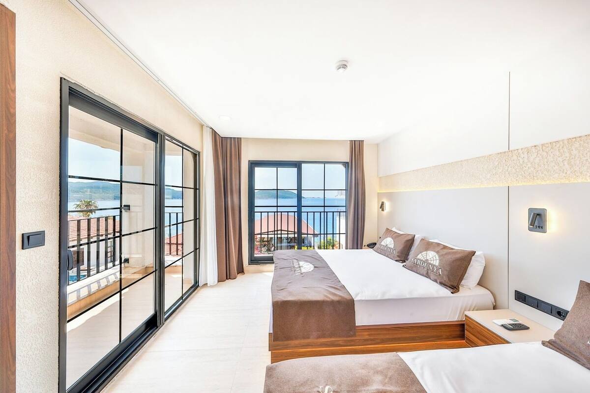 A hotel room with a balcony, a bed, a bedside table, and a view of the sea.