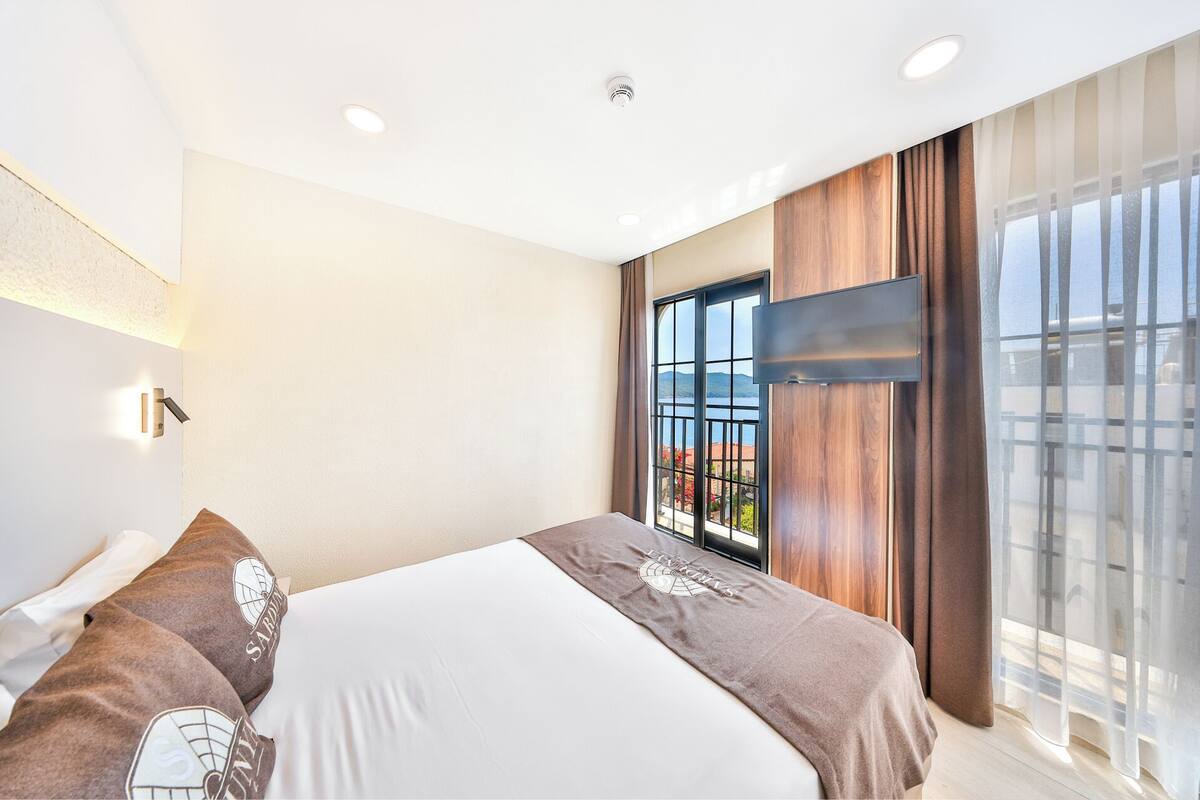 A modern hotel room with a large bed, a TV mounted on the wall, and a balcony with a view.