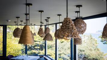 Comedor con lámparas de mimbre colgantes y vistas a árboles y agua a través de amplias ventanas.