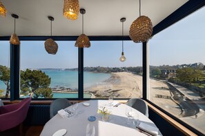 Un coin repas avec une table dressée pour quatre personnes, offrant une vue sur la plage et la mer.