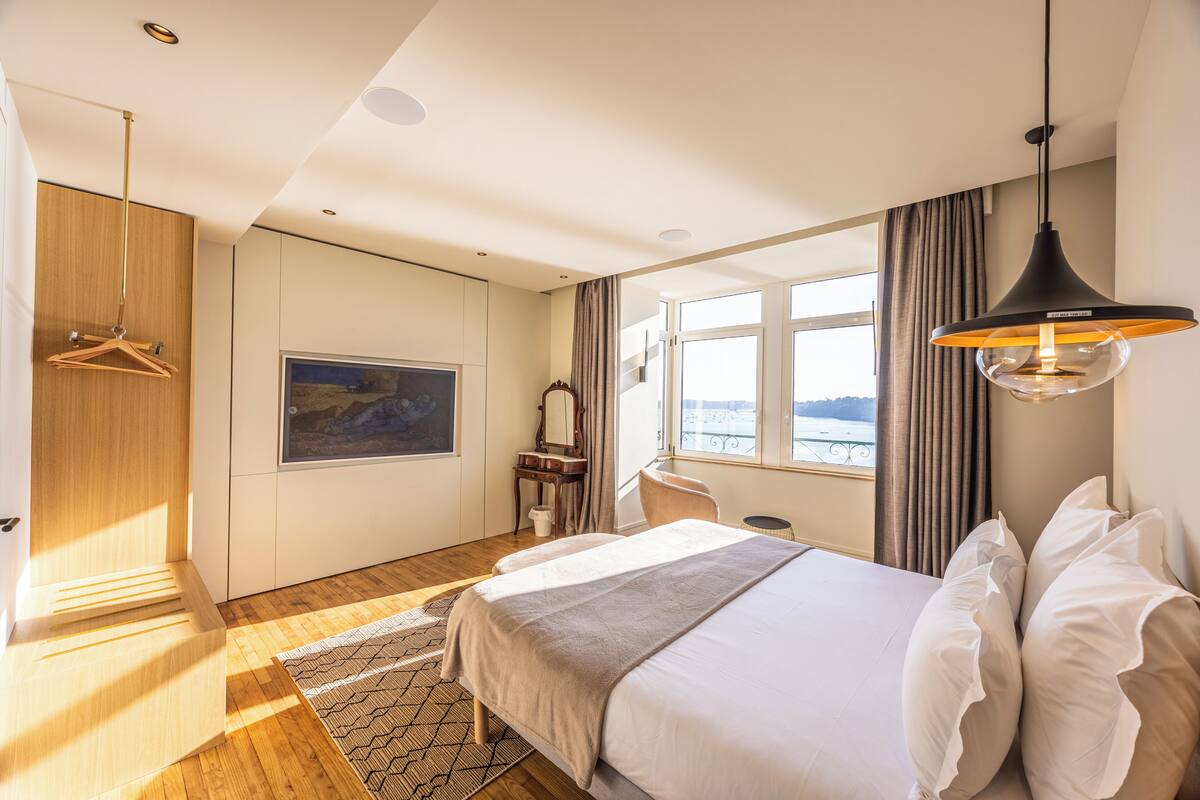 A modern hotel room with a large bed, a desk, and a view of the sea.