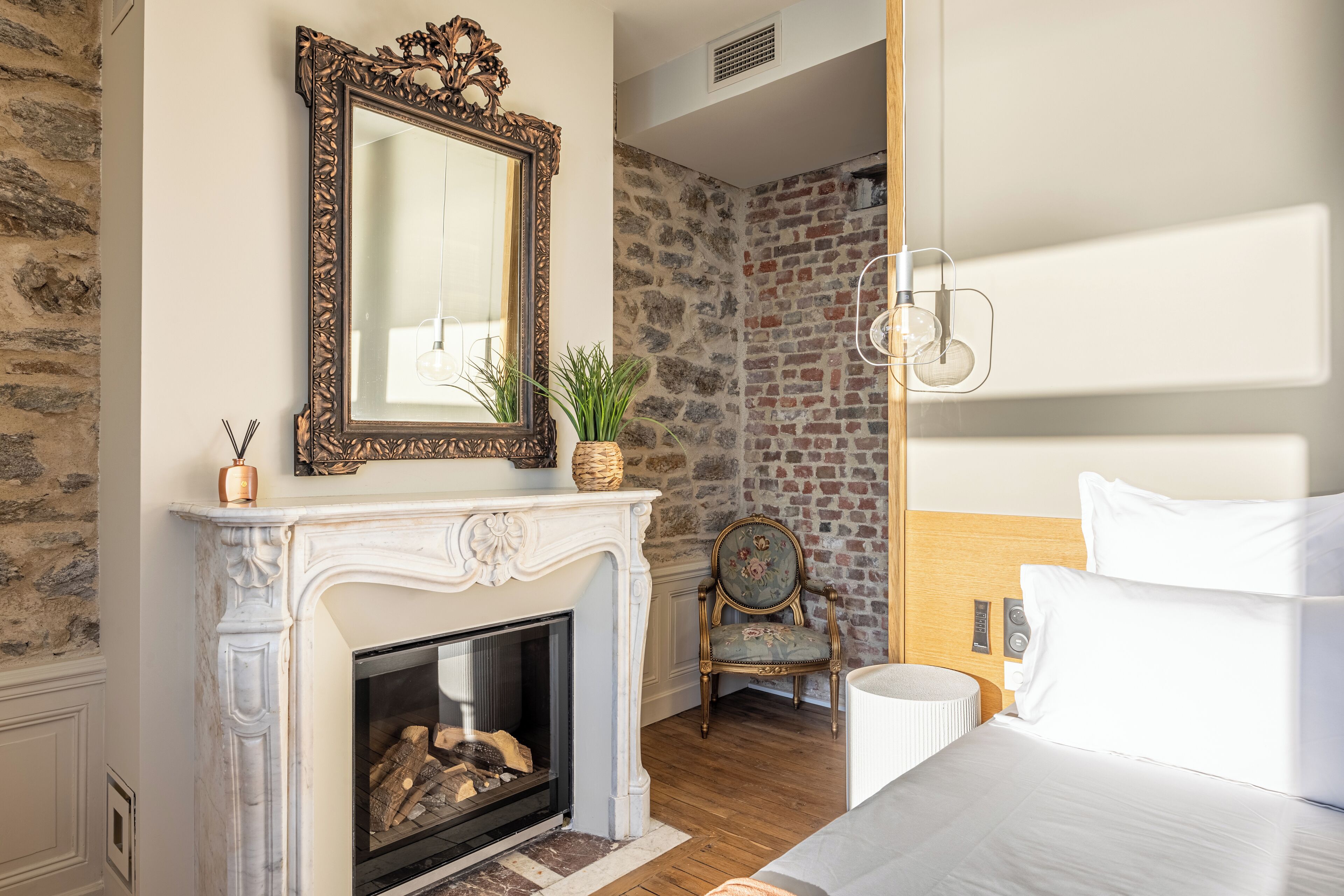 A bedroom with a fireplace, a mirror, a chair, and a bed.