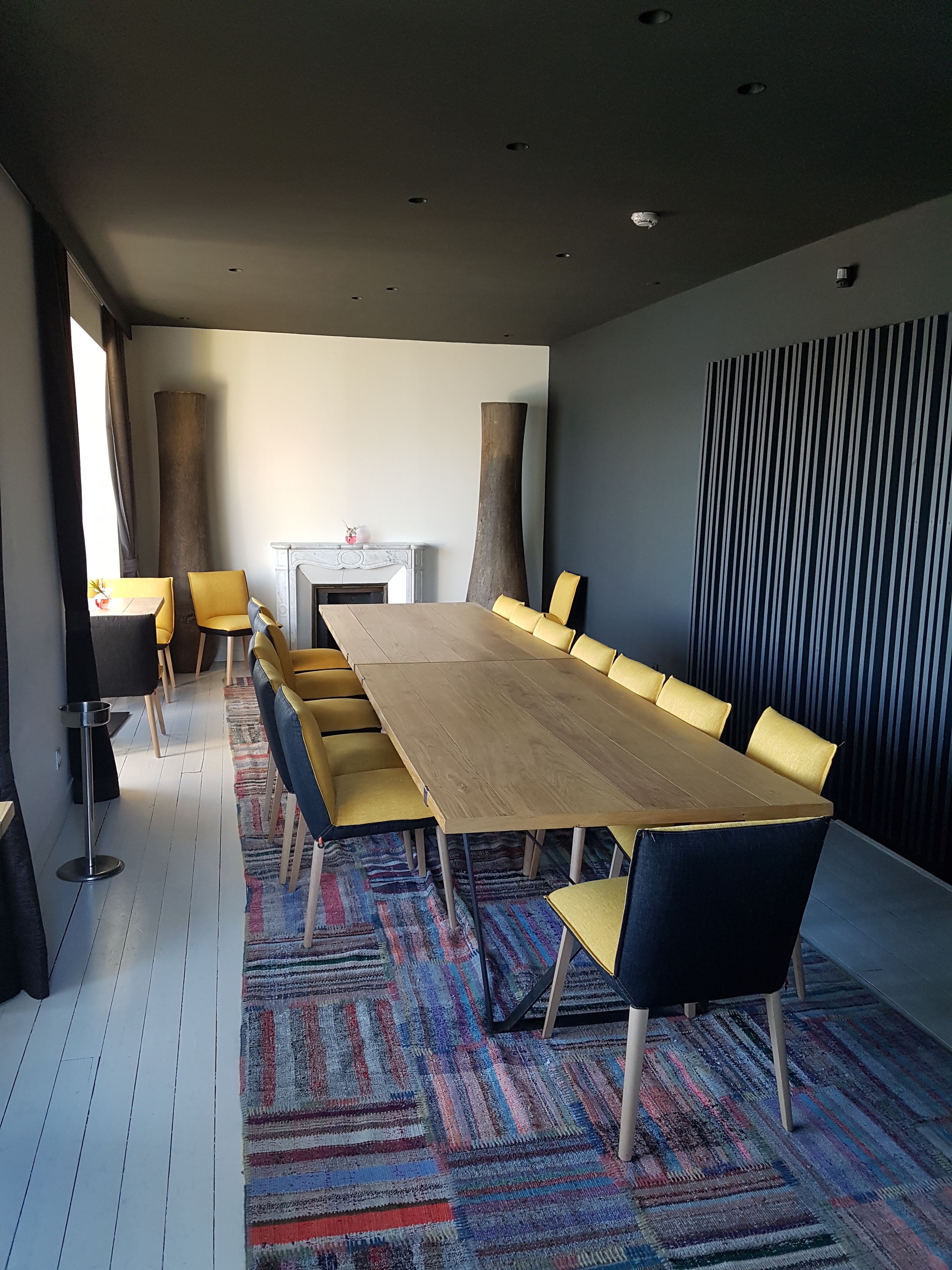 A conference room with a long wooden table, yellow chairs, and a patterned carpet.