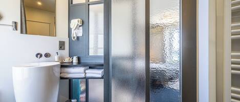 Un baño con un lavamanos grande y blanco, un espejo, un perchero para toallas y una puerta de cristal con paneles satinados.