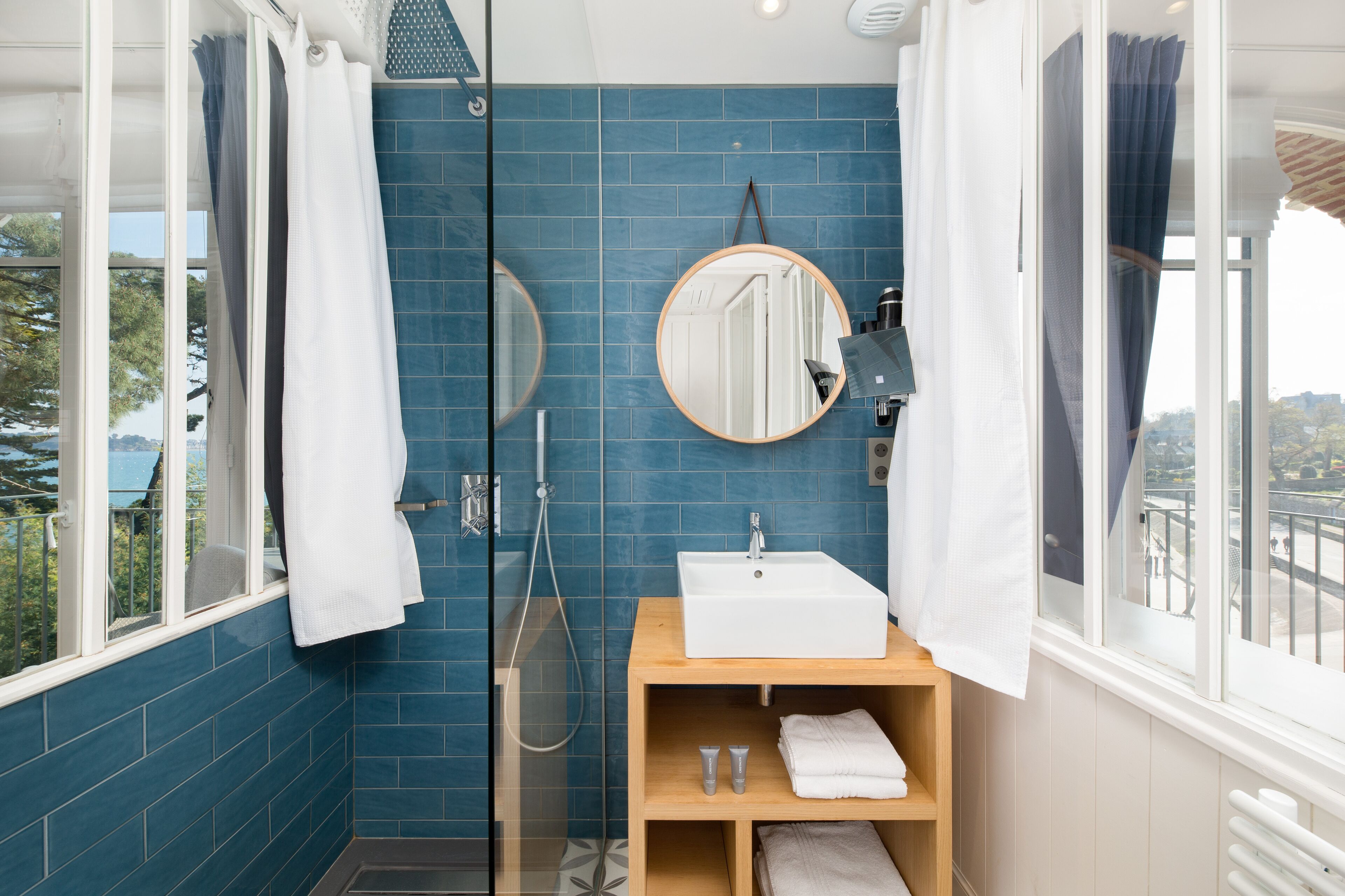 Un baño con pared de azulejos azules, un lavamanos blanco, un espejo y una ducha.