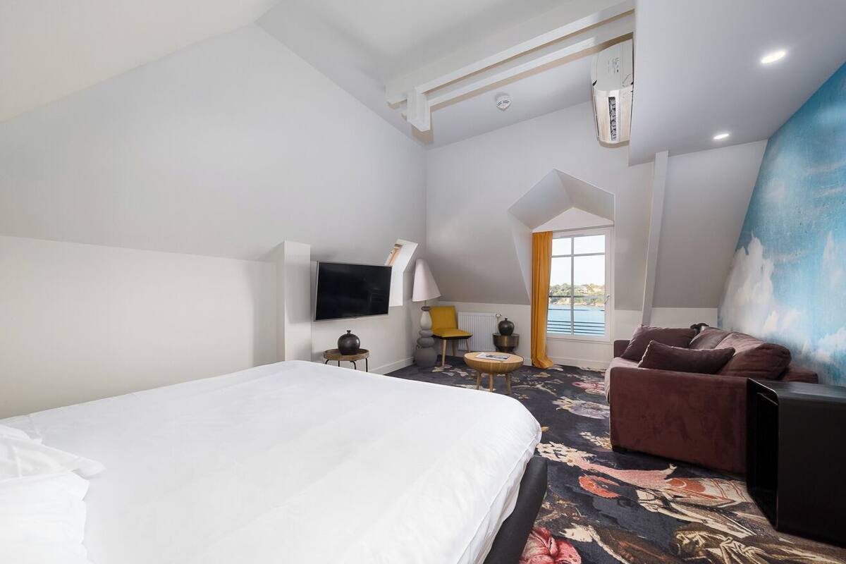 A hotel room with a large bed, a sofa, a TV, a small table, and a painting on the wall.