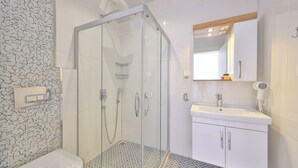A modern bathroom with a glass-enclosed shower, a white sink, and a patterned floor. - Sardunya Andifli Otel (Kas)