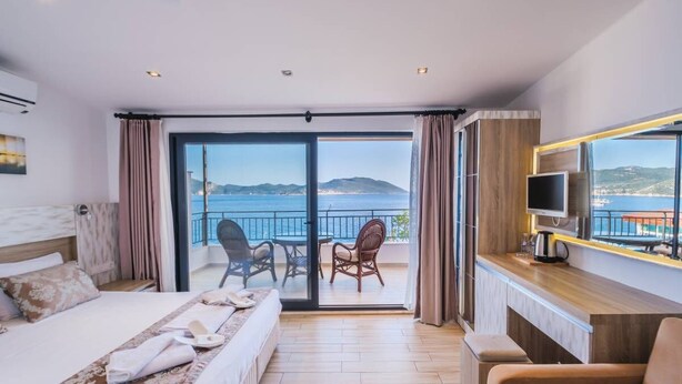 A hotel room with a bed, a TV, a balcony with a view of the sea, and a dining area. - Sardunya Andifli Otel (Kas)