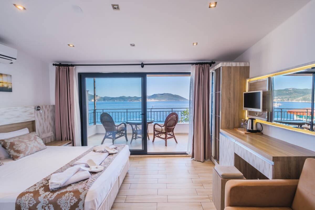 A hotel room with a bed, a TV, a balcony with a view of the sea, and a dining area.