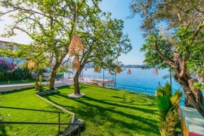 A landscaped garden with a pathway leading to a seating area, overlooking a body of water. - Sardunya Andifli Otel (Kas)