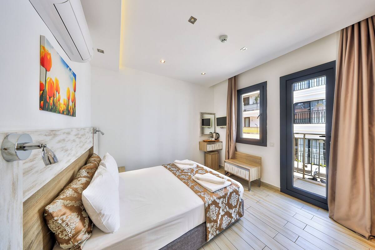 A hotel room with a bed, a bathroom, a window with a view, and a painting on the wall.