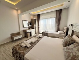 Una habitación de hotel con una cama grande, un escritorio con una computadora, una silla, un ventanal con cortinas y un cabecero con espejo.