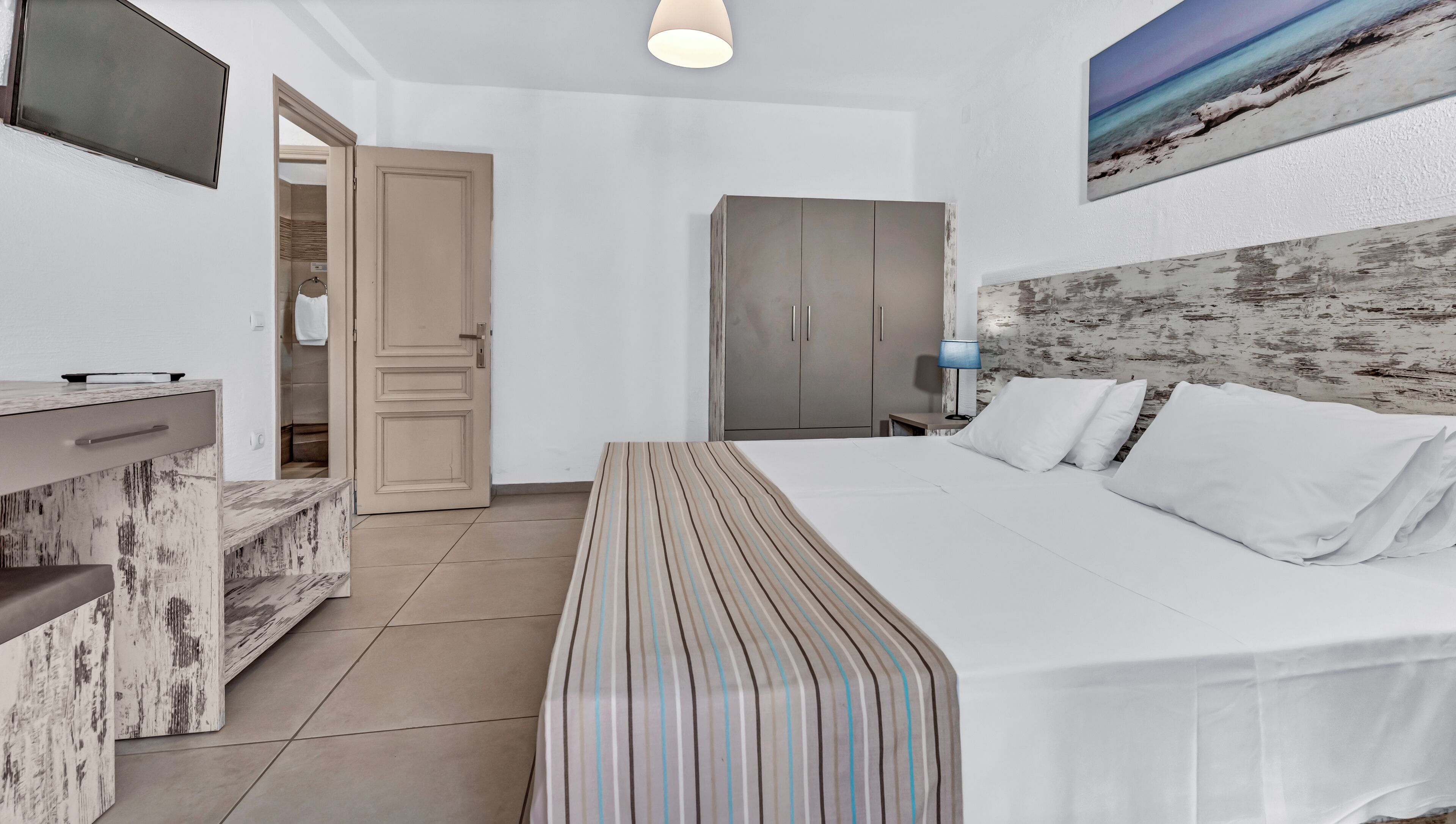 Una habitación de hotel con cama, escritorio, armario y televisor.