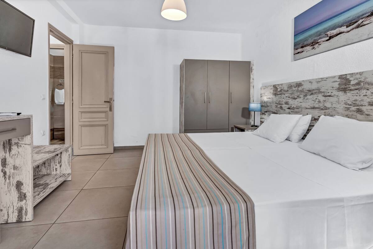 A hotel room with a bed, a desk, a wardrobe, and a painting on the wall.
