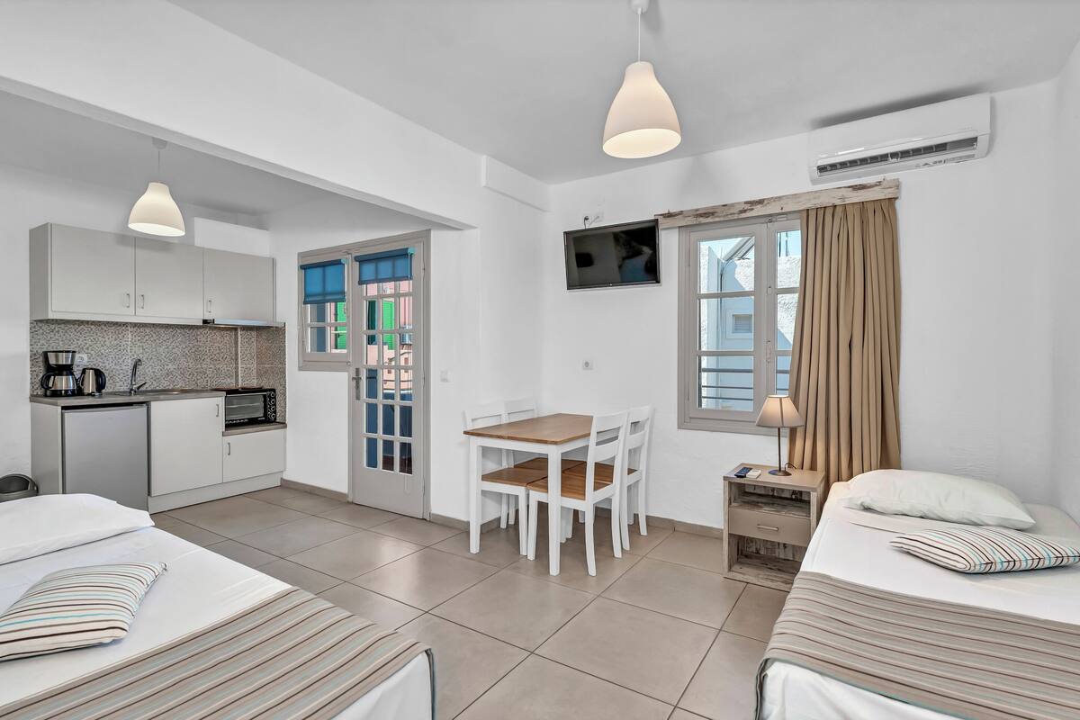 A modern hotel room with a kitchenette, a dining area, and two beds.