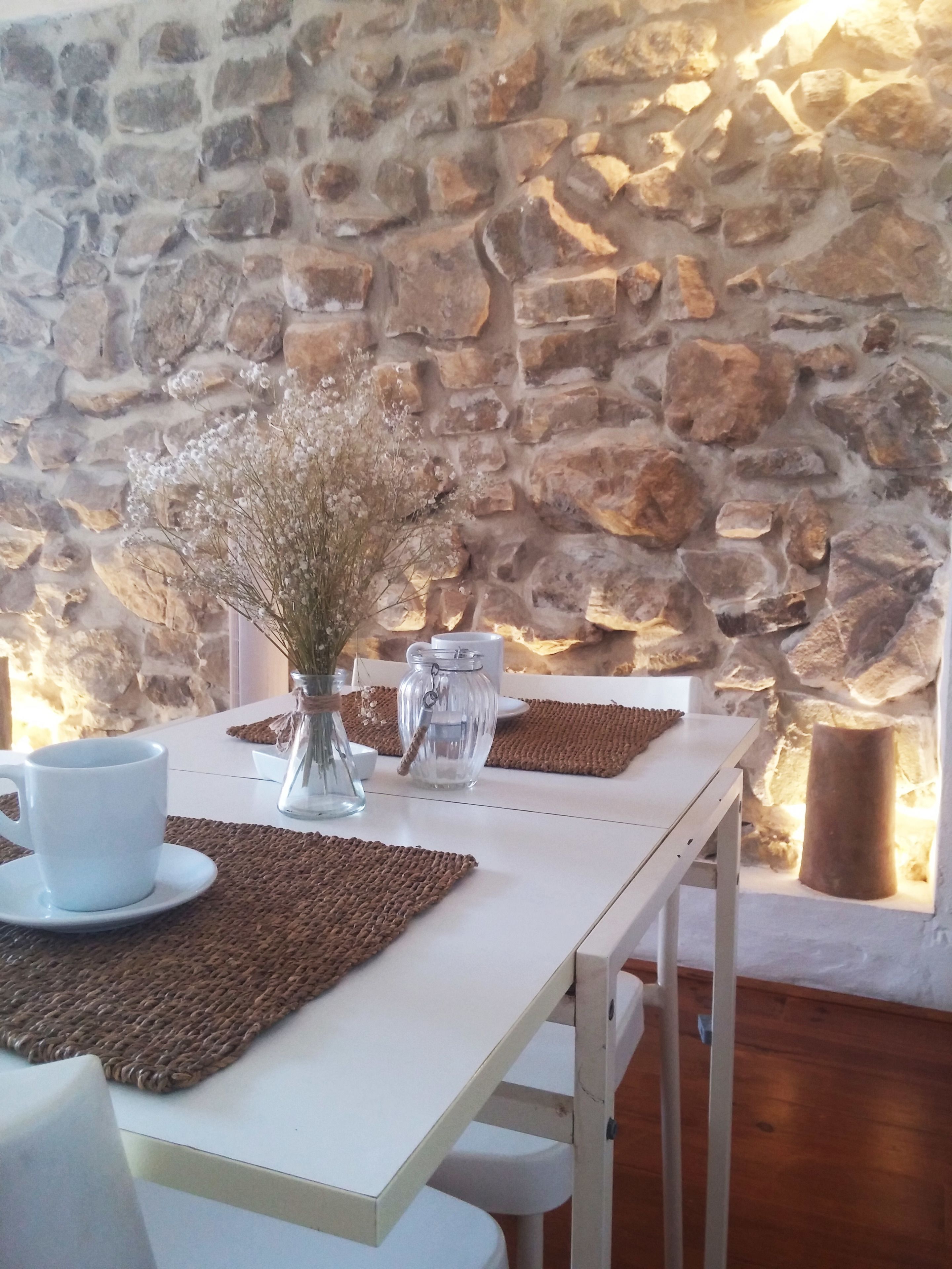 A dining area with a stone wall, white table, and brown placemats.