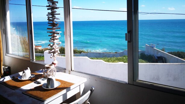 A room with a large window overlooking the ocean, a table with a white tablecloth, and a decorative spine structure. - Bungalows Castillejos - Adults Only (Barbate)