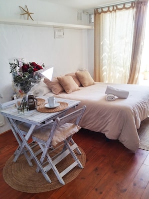Ein gemütliches Zimmer mit Holzboden, einem Bett mit beigefarbener Bettwäsche, einem Tisch mit einer weißen Lampe und einem Stuhl.