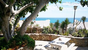 A stone patio with a white picnic table, surrounded by potted plants and a view of the sea. - Bungalows Castillejos - Adults Only (Barbate)