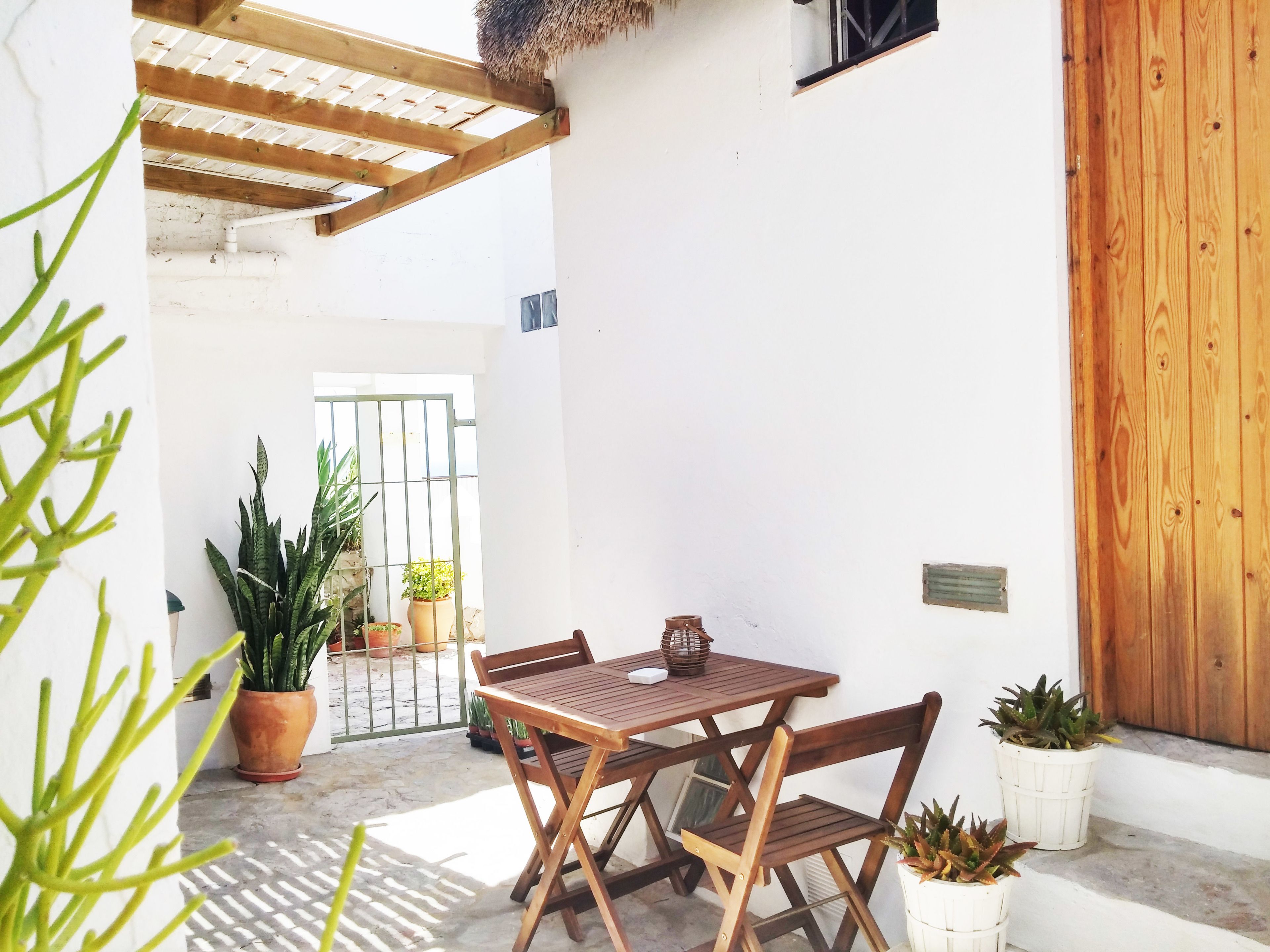 Mesa y sillas de madera en un espacio exterior cubierto con plantas en macetas.