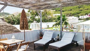 A covered outdoor seating area with lounge chairs and a table, overlooking a pool and greenery. - Bungalows Castillejos - Adults Only (Barbate)
