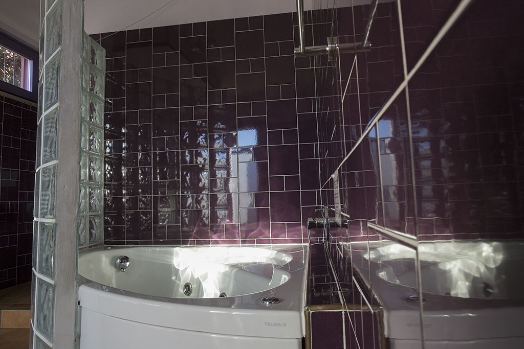 Un baño moderno con una bañera acristalada, un espejo grande y un revestimiento de pared de baldosas negras.