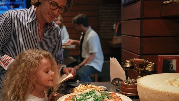Interior de restaurante con una pizza, aceitunas y pepinillos en la barra.
