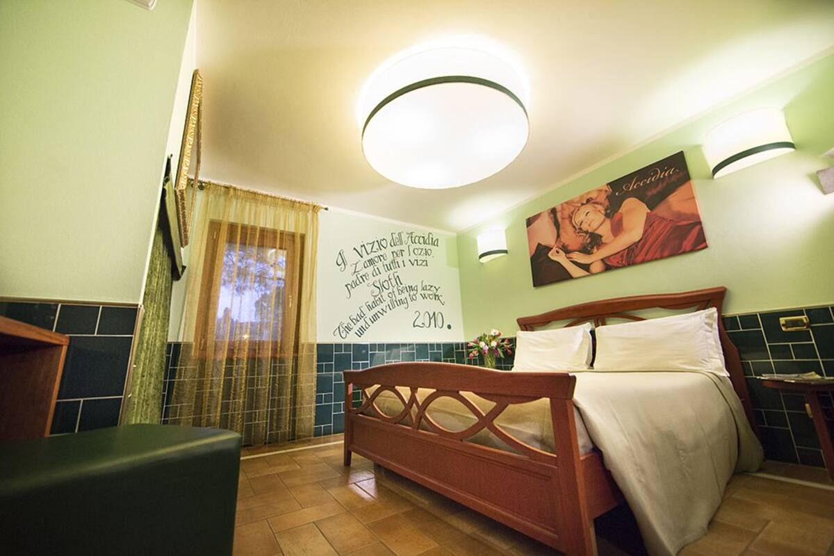 A hotel room with a bed, a wall with a poster, a window with curtains, and a bathroom area.