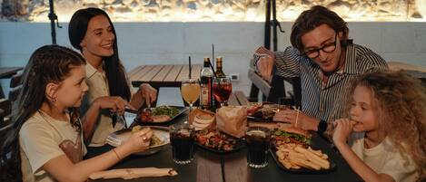 A group of people dining at an outdoor table with various dishes and drinks.