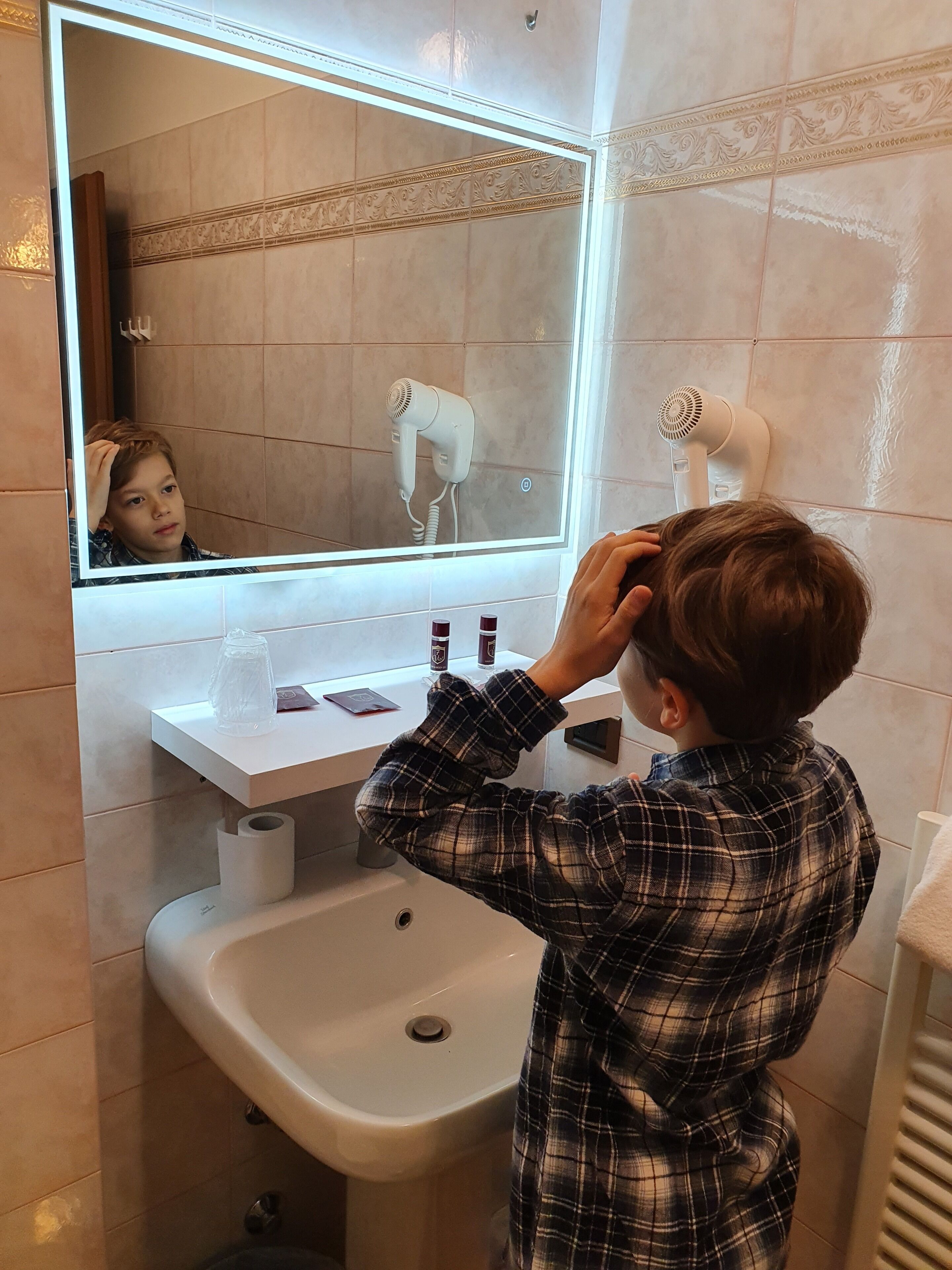A bathroom with a mirror, a sink, and two hair dryers mounted on the wall.