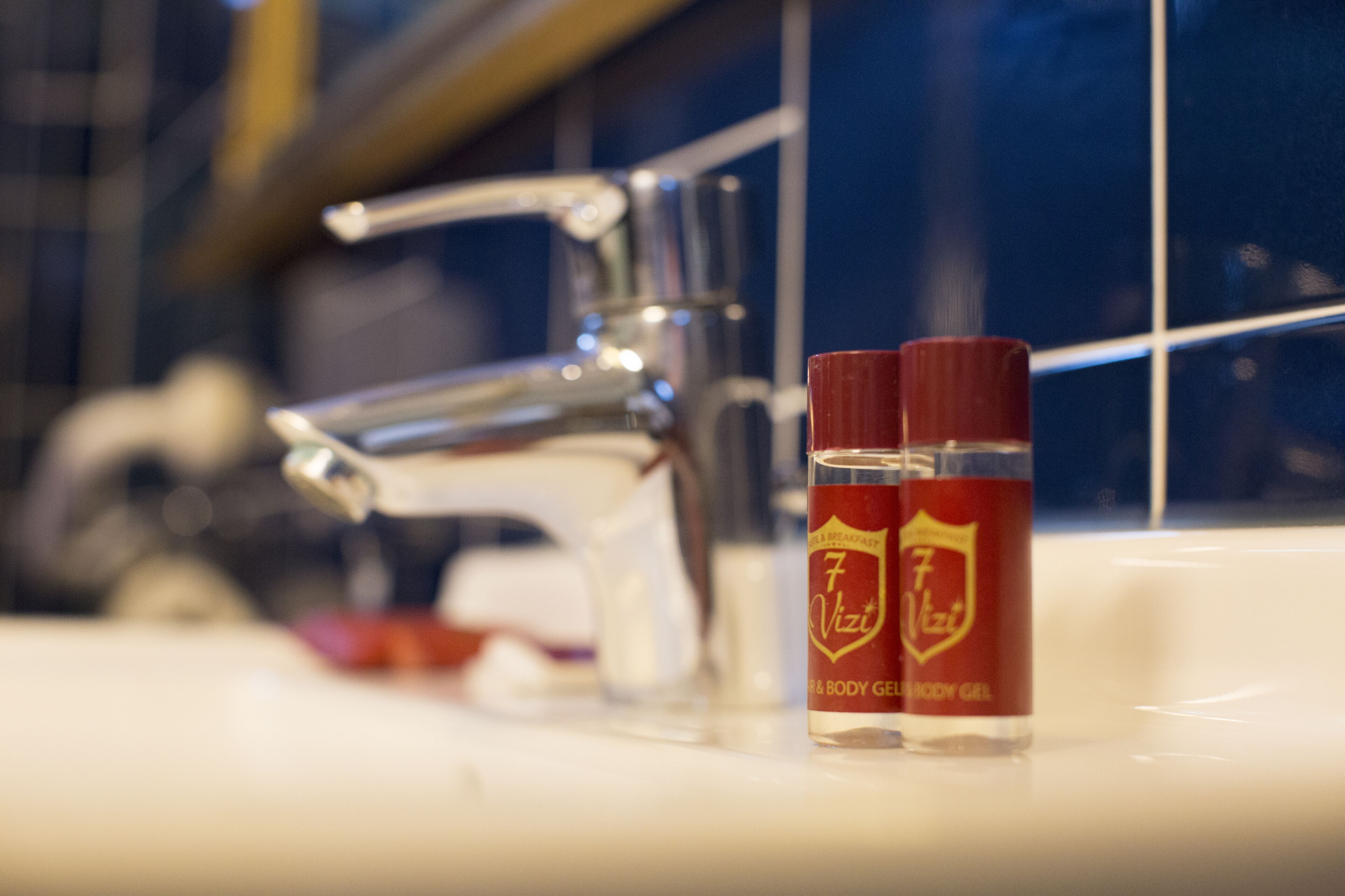 A bathroom sink with a chrome faucet and two red bottles labeled "7 Vizi" on a white countertop.