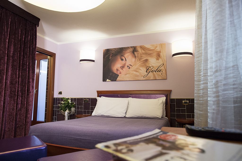 Habitación de hotel con una cama grande, dos mesitas de noche, una lámpara de pared e un cartel en la pared.