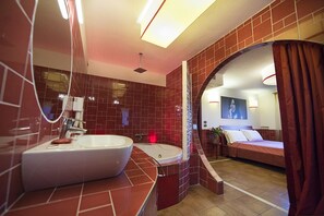 A modern bathroom with a large sink, a shower, and a mirror. There is a bed with a view of the room in the background. - Suite & Breakfast 7 Vizi (Lazise)