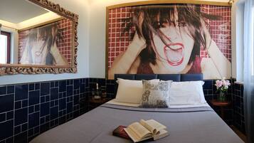 A hotel room with a large bed, a nightstand, a mirror, and a wall with a large artwork.
