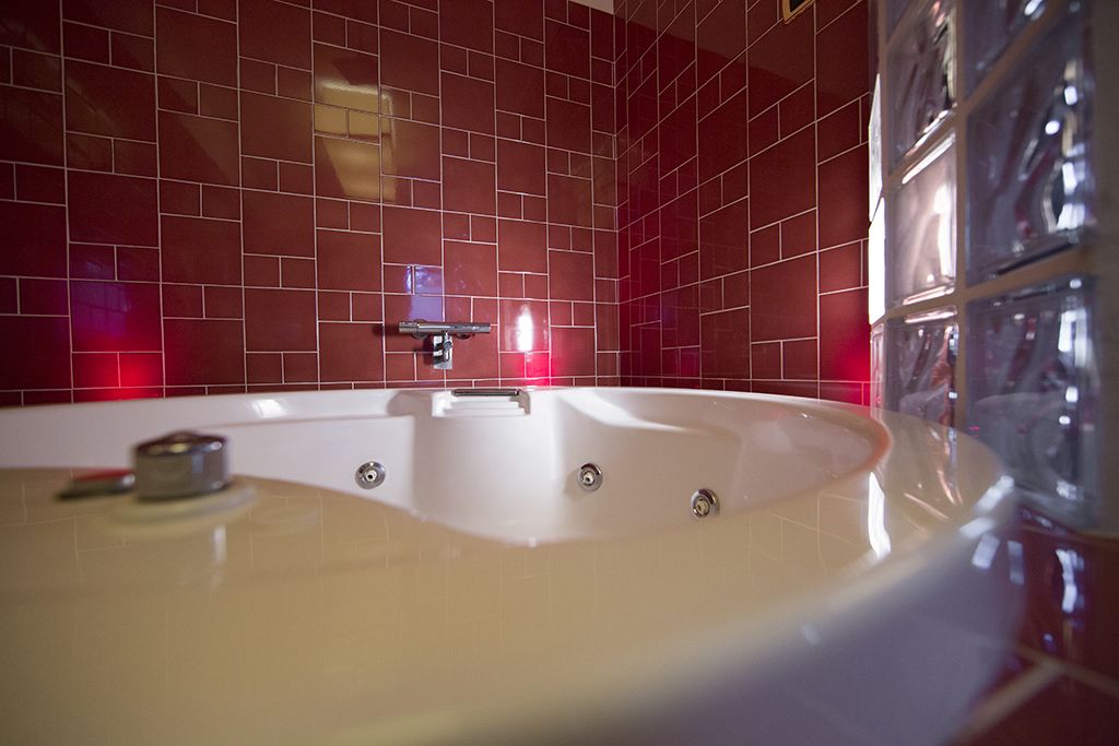 A modern bathroom with a large bathtub, red tiled walls, and a glass shower enclosure.