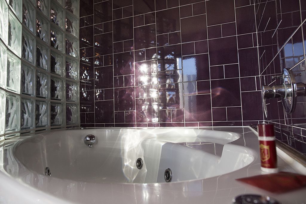 A modern bathroom with a large bathtub, dark tiled walls, and a glass shower enclosure.