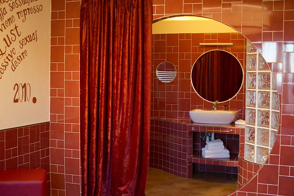 Een badkamer met rode betegelde wanden, een ronde spiegel, een wit wastafel en een rood gordijn.