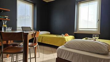 Una habitación de hotel pequeña con una cama, un escritorio con una computadora portátil, una silla y una ventana.