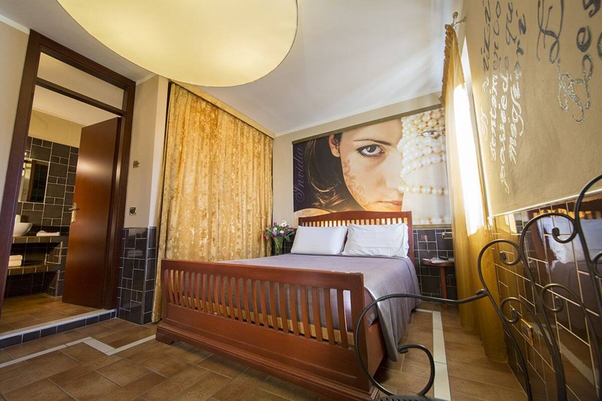 A bedroom with a wooden bed, a large wall mural, a bathroom with a tiled shower, and a circular ceiling light.