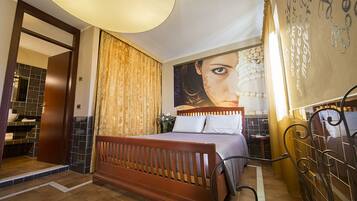 A bedroom with a wooden bed, a large wall mural, a bathroom with a tiled shower, and a circular ceiling light.