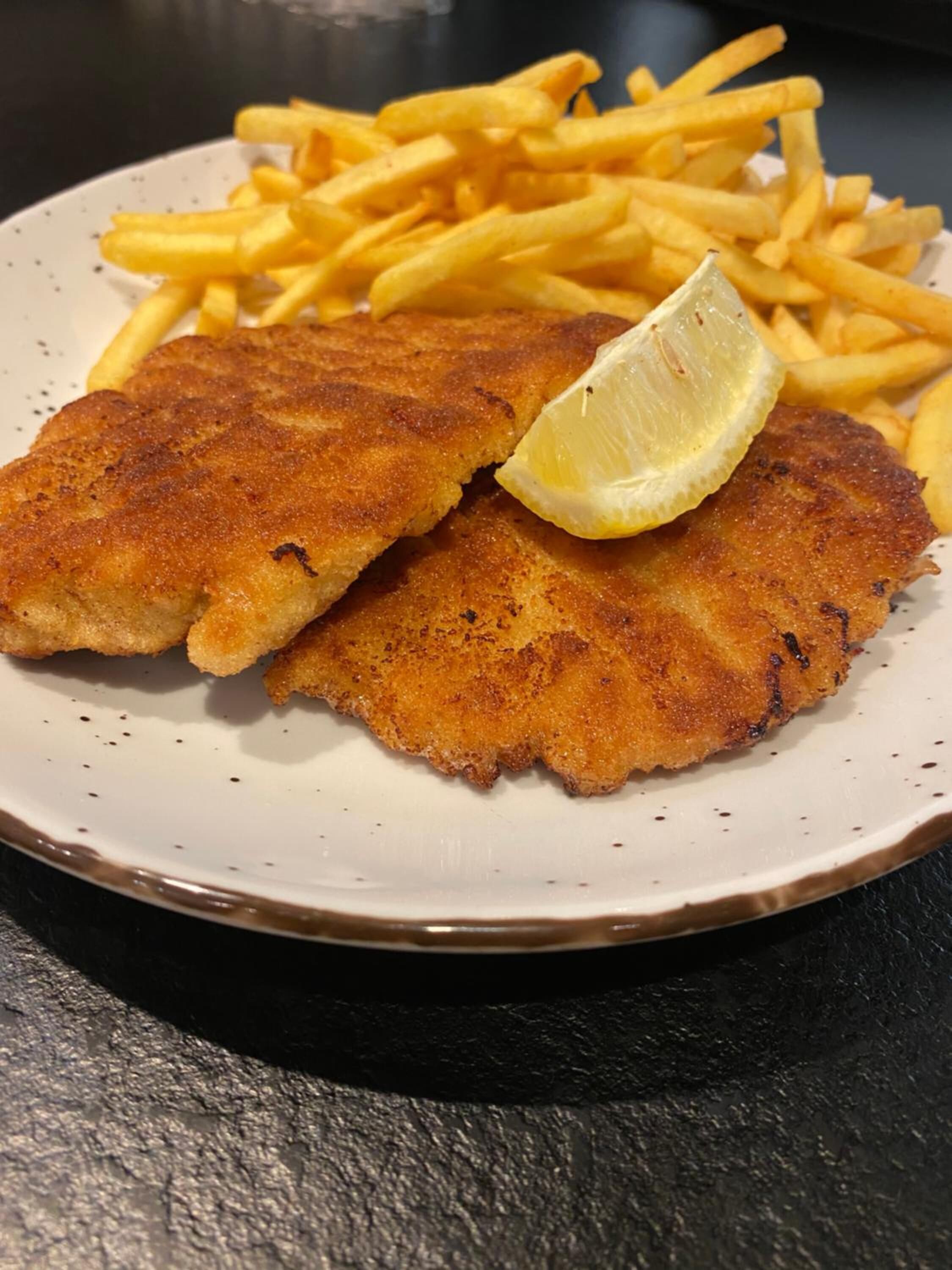 A plate with breaded fish fillets and French fries, accompanied by a lemon wedge.