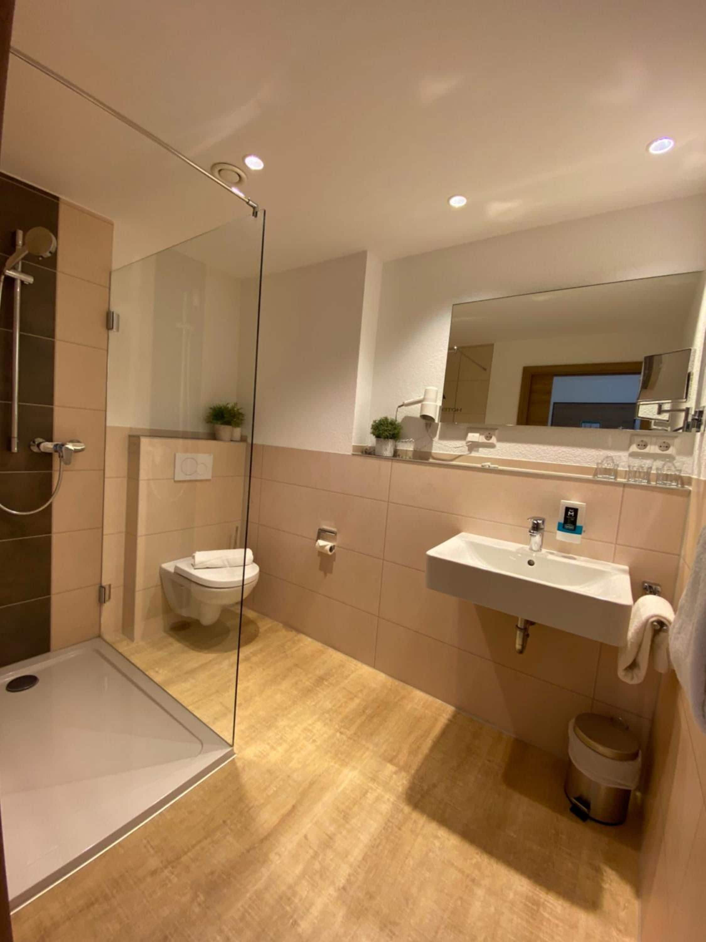 Un baño moderno con cabina de ducha de vidrio, inodoro, lavabo con espejo y cubo de basura.