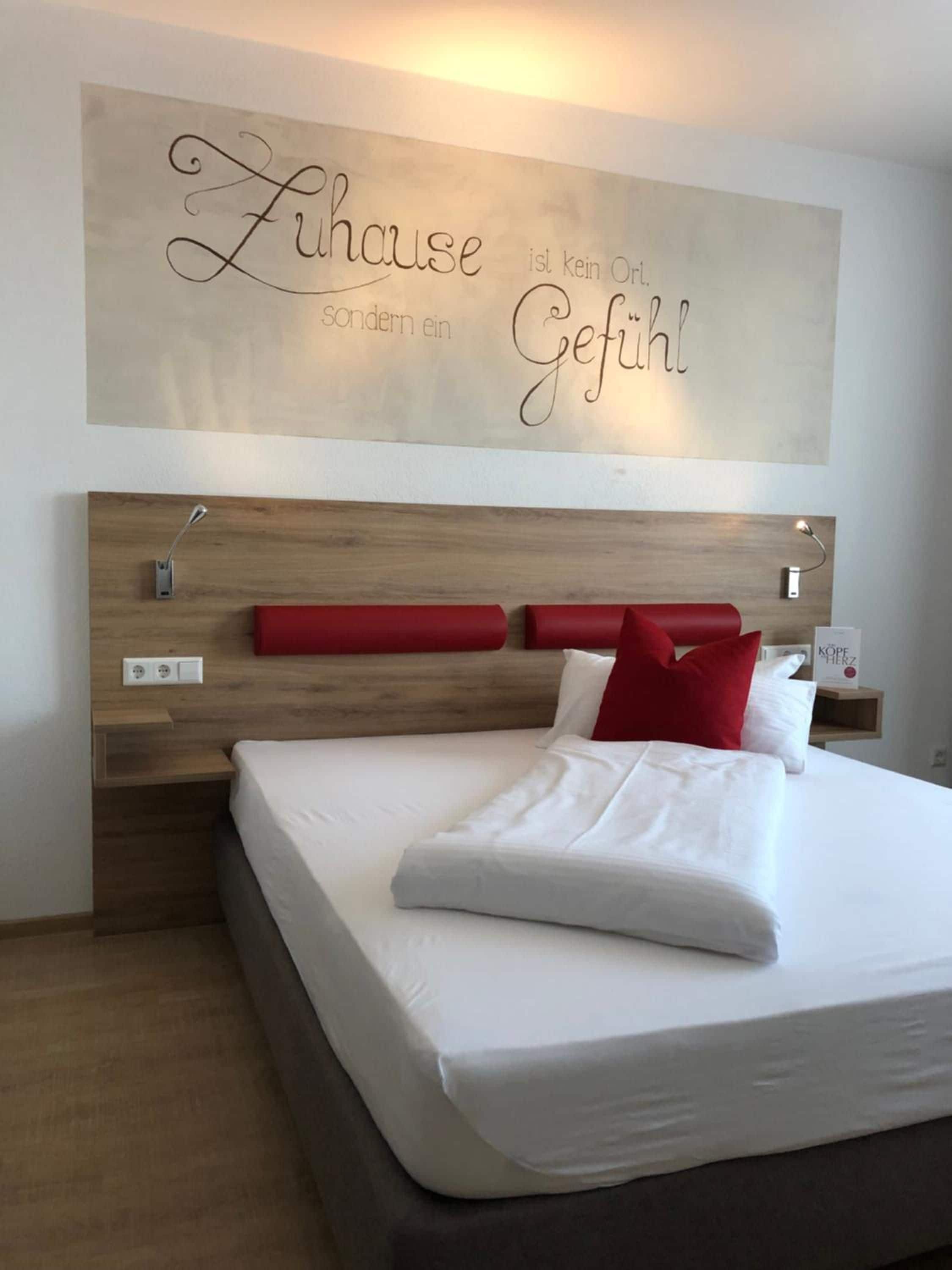 Habitación de hotel con una cama grande, cabecera de madera y una pared con una frase motivacional.